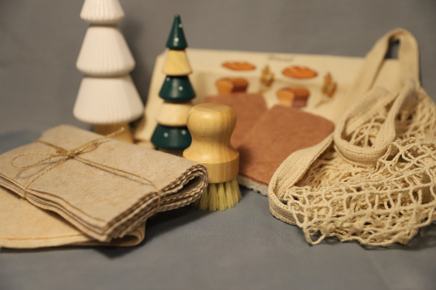 Set of eco-friendly products including a brush, cloth, and mesh bag on a gray surface.